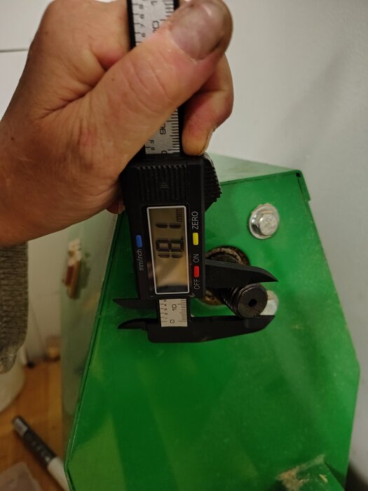 Person mäter gängor på en maskindel med skjutmått över en grön yta.