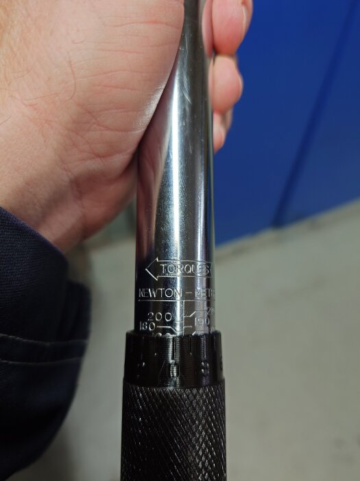 Inzoomad bild av en momentnyckel med skalan inställd på 180 Nm. En hand håller i nyckelns handtag.