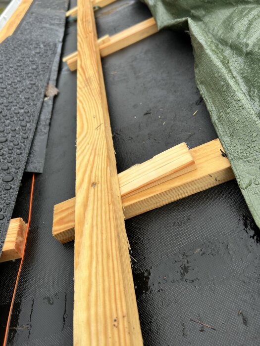 Takterrass med träreglar under en grön presenning, delvis exponerade, med fukt och droppar på ytan.