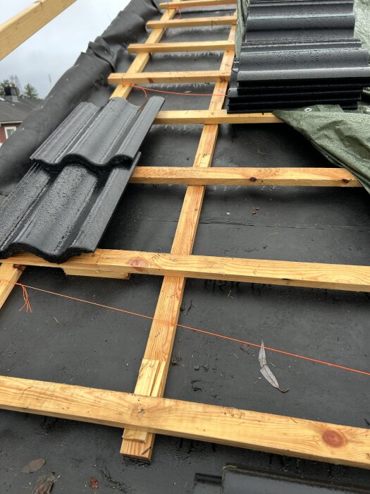 Tak under byggnation med träreglar och takpannor, delvis täckt av en presenning.