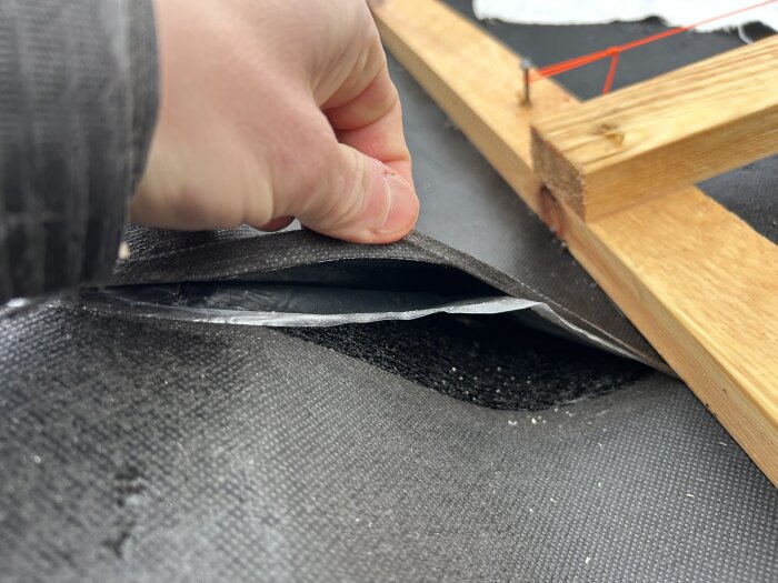 Hand lyfter presenning på taket, träreglar syns.