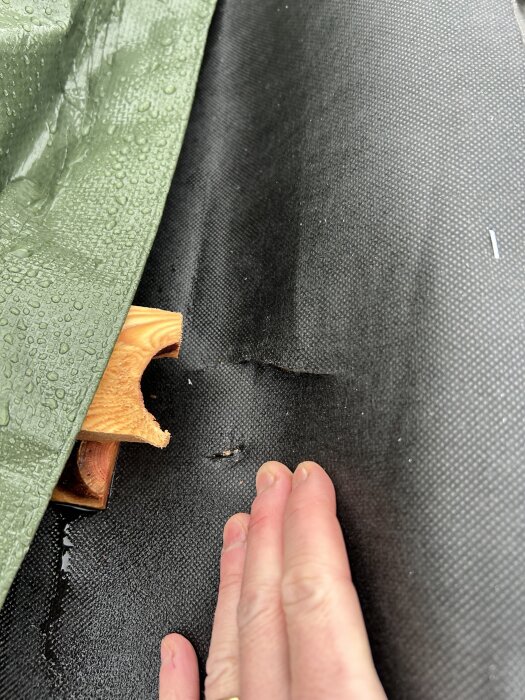 Hand vid presenning över svart material och träbit.