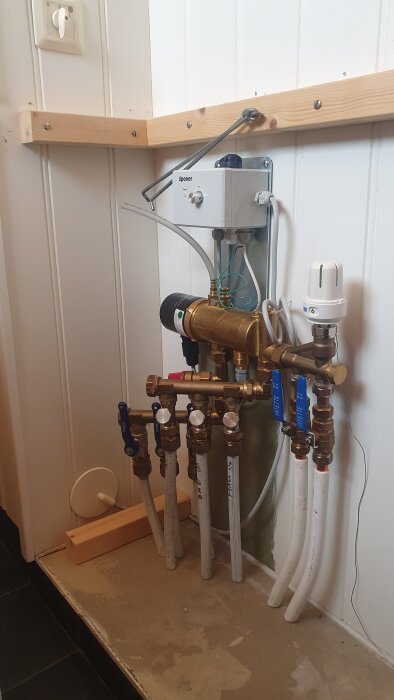 Cirkulationspump och rörsystem för golvvärme monterat på vägg inuti en byggnad.