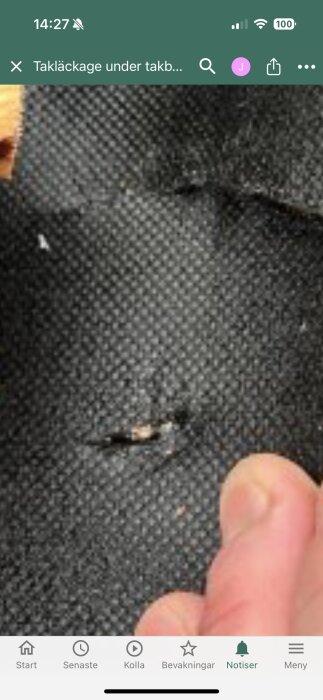 Skadat takmaterial med ett hål, där en person pekar, vilket kan orsaka läckage.