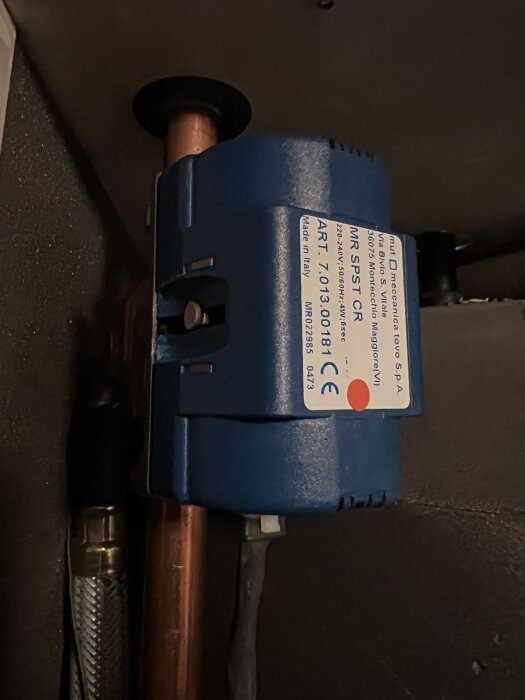 Blå manuell växelventil installerad på ett kopparrör, med etikett som visar modell och specifikationer, del av ett värmesystem.