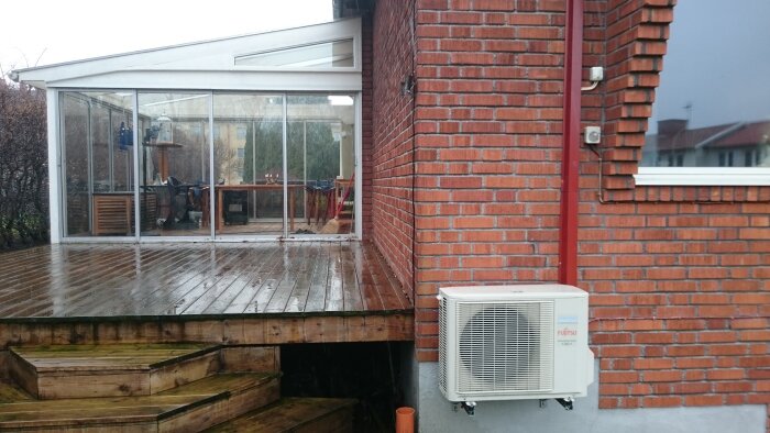 Uterum med glaspaneler och trätrall, anslutet till ett rött tegelhus. Dränering utförd nära väggen, jorden grävd ner till trallen.