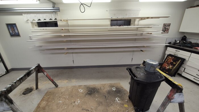 Vitmålad list och foder på hyllor i ett hobbyrum med målarburk och verktyg.