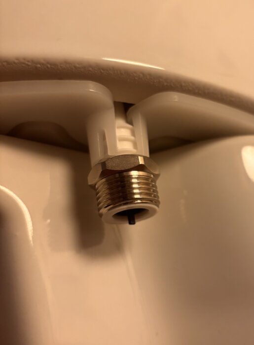 Närbild av en halvkoppling på en toalett, sett snett underifrån med fokus på kopplingsdetaljer i metall och plast.