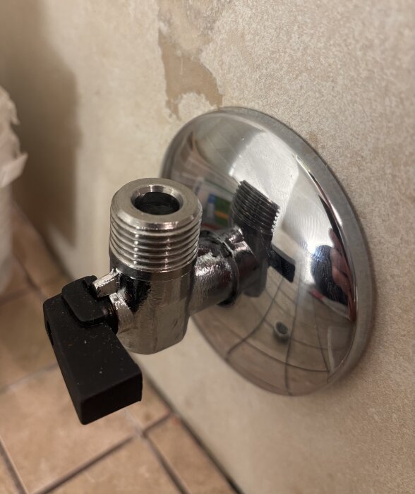 Kromad vattenanslutning med svart vred på en badrumsvägg, eventuellt en LK-halvkoppling för toaletten.