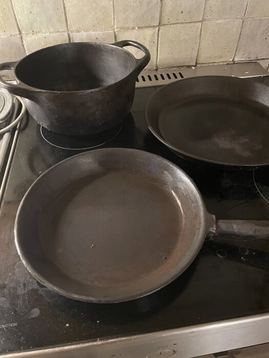 Tre gjutjärnskärl, inklusive två stekpannor och en gryta, på en spis.