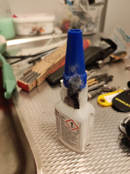 Flaska med blått lock av cyanidlimmet Loctite 406 stående på arbetsyta, med diverse verktyg och material omkring.