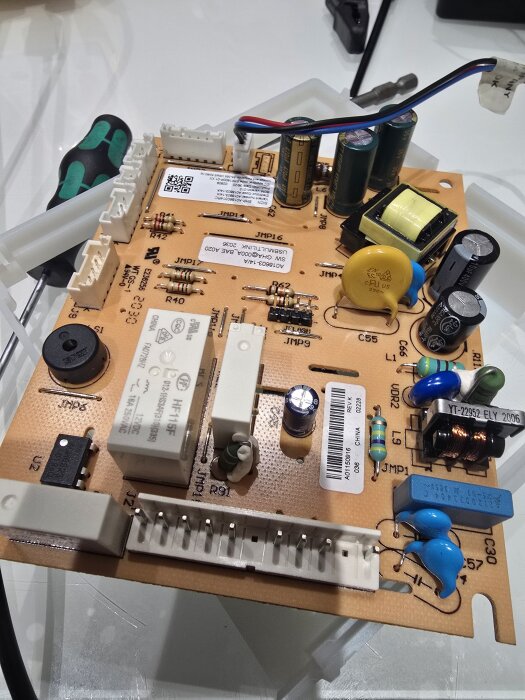 Elektroniskt kretskort med olika komponenter, inklusive kondensatorer, motstånd och kopplingar, ligger på ett vitt bord bredvid en skruvmejsel.