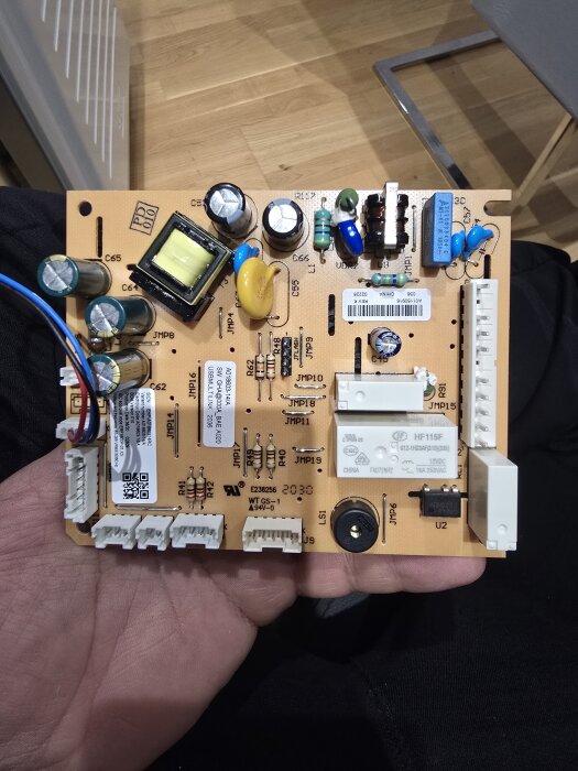 Kretskort med komponenter som kondensatorer, motstånd och kopplingar hålls i en hand. Bakgrund av trägolv.