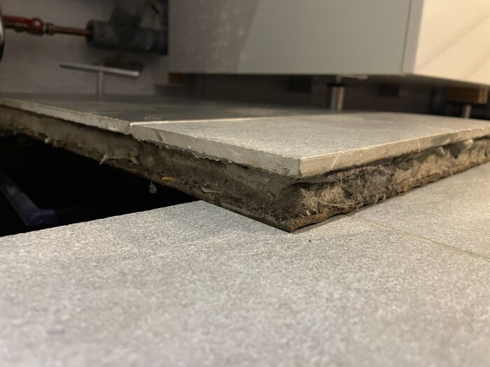 Lyft klinkerplatta demonterad från golv, visar underliggande fix och konstruktion nära ett skåp.