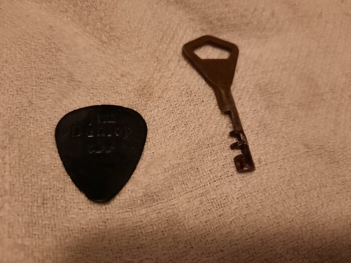 En gitarrplektrum och en metallnyckel ligger intill varandra på en vit tygbakgrund.