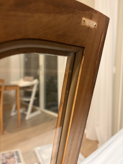 Gammalt vitrinskåp med glasdörr, närbild på hörn med gummilist, skåpet står i ett rum med trägolv och vita gardiner i bakgrunden.