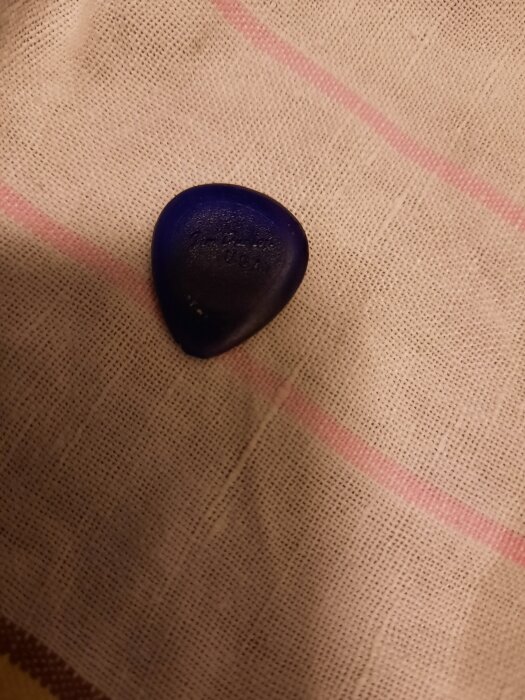 Blått gitarrplektrum på beigebrun randig duk.