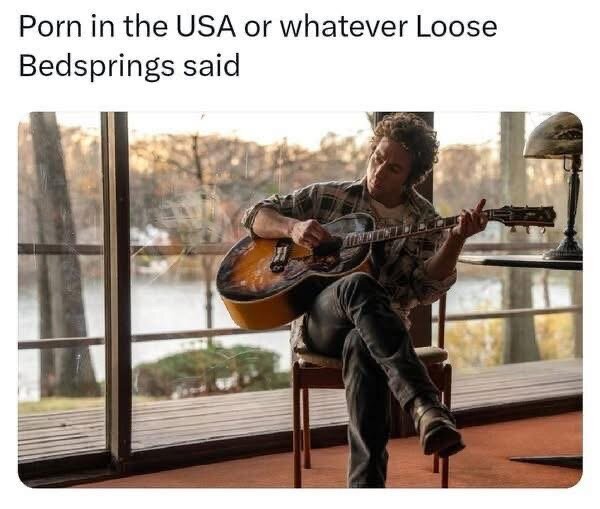 En person sitter på en stol och spelar gitarr framför ett stort fönster med träd utanför.