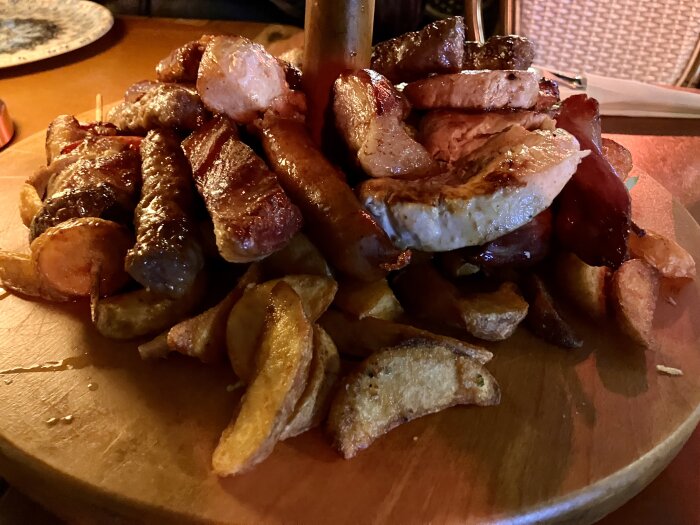 Assiett fylld med grillat kött, korvar och klyftpotatis.