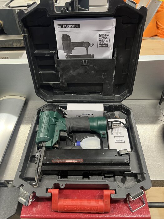Dyckertpistol av märket Parkside i en öppen svart verktygslåda med tillbehör och en manual, placerad på ett bord.