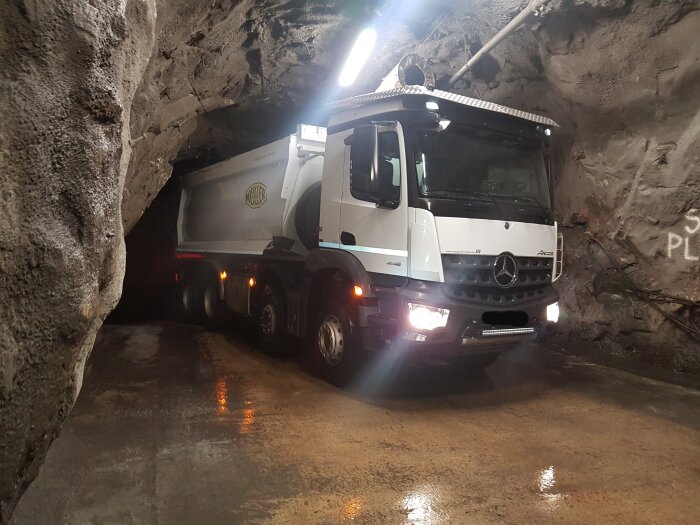 Lastbil inne i en trång tunnel, med grova bergväggar och blanka ljusreflexer på golvet.
