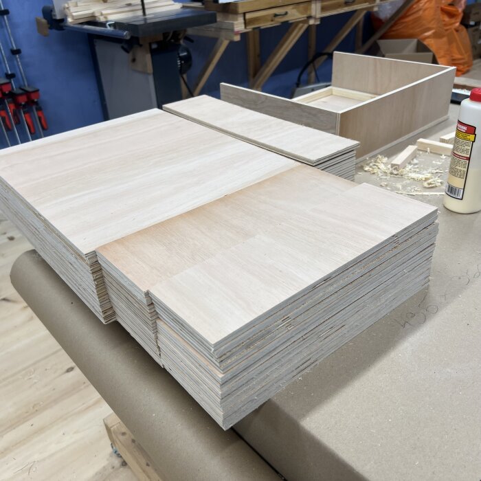 Staplar av träskivor och plywood redo för byggande av lådor i en verkstad.