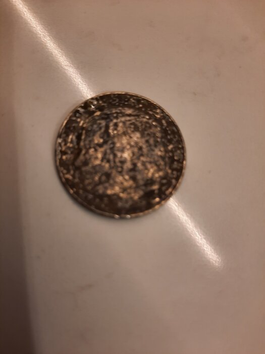 En närbild av ett slitet mynt liggande på ett bord, otydligt motiv på myntet.