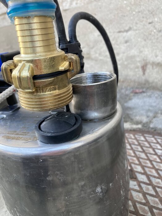 Guldfärgad pumpanslutning med kort gänga, oansluten metallförskruvning, svart backventil synlig, monterad på metallcylinder mot betongbakgrund.