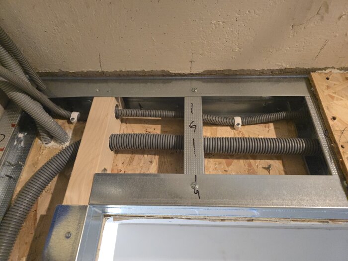 Flexrör och stålreglar över en dörröppning i ett pågående byggprojekt. Synliga träreglar och skivmaterial i bakgrunden.