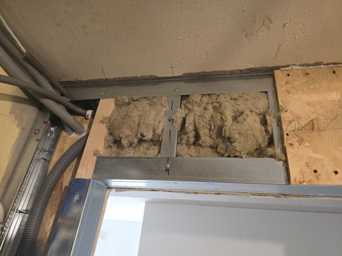 Flexrör och isolering installerade över en dörröppning med synliga reglar och oskyddad isolering vid ett renoveringsprojekt.