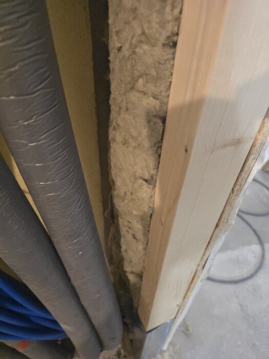 Isolering och träregel monteras vid sidan av grova rör och kablar i ett pågående renoveringsprojekt för hobbyrum/gym.