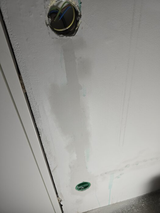 Vägg med spacklat nytt eluttag, flexrör synligt. Spår av torkad färg eller vatten på väggen. Förberett för målning i hobbyrum/gym.
