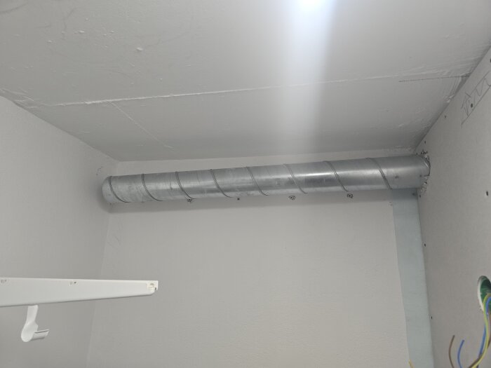 Spirorör monterat i hörnet av ett rum med vitmålade väggar och tak, elektriska kablar synliga i nederkant.