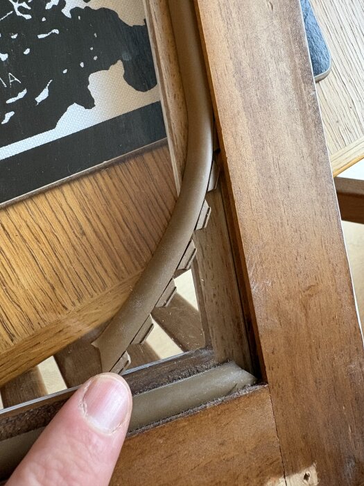 Trälist monterad i skåra på fönsterkarm, delvis lossad och pekas på av ett finger på en träyta.