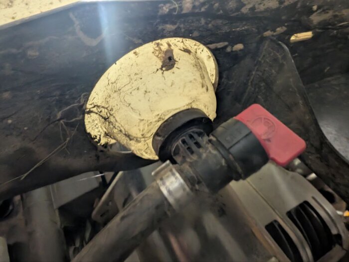 Bensinkran med röd ventil inuti smutsigt motorutrymme, ventilen kan vara öppen och eventuellt icke-tät.