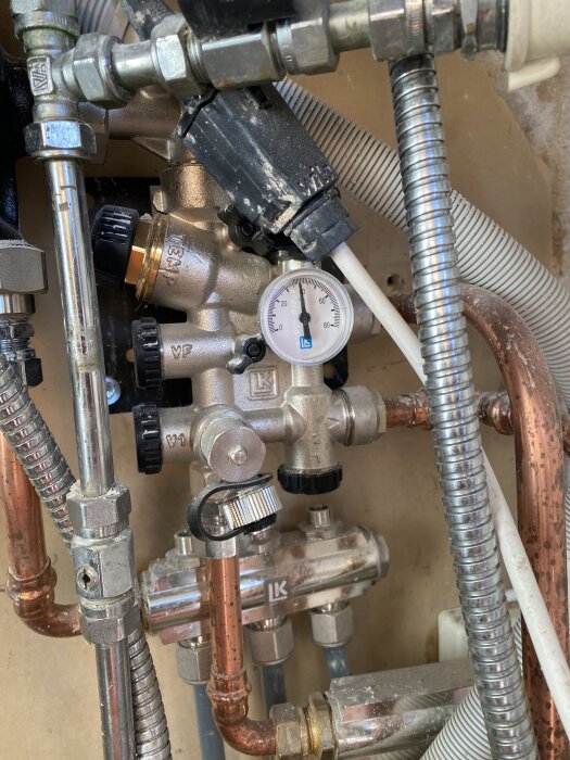 Bilden visar ett rörsystem med kopparrör, termostatventiler och en tryckmätare som visar ungefär 45 grader Celsius.