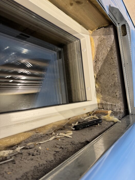 Fönsterkarm i källare med synlig betong, isolering och ett verktyg. Konstruktionen visar luftspalt och reglar innan gipset sätts på plats.