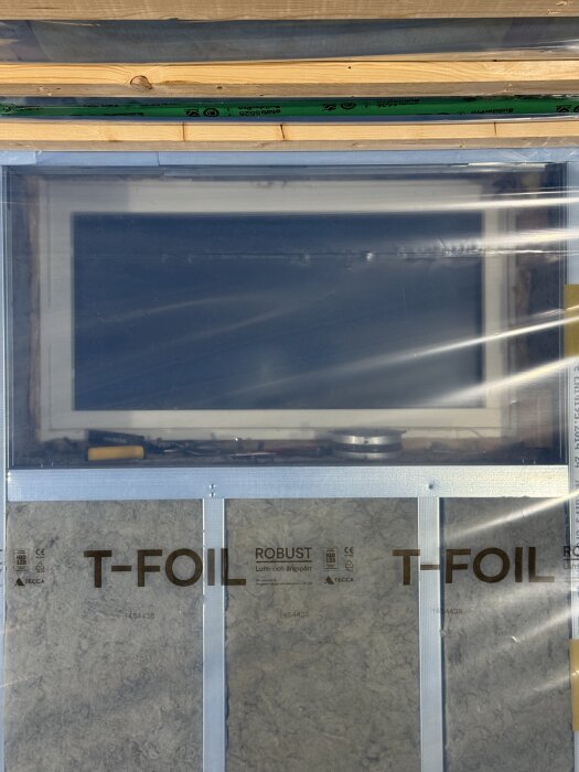 Fönster i källare med T-Foil isolering monterad på stålreglar, omgiven av byggmaterial som förbereds för att sätta gips.