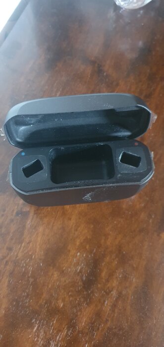 Svart behållare med öppet lock och tre fack för apparater på ett träbord.