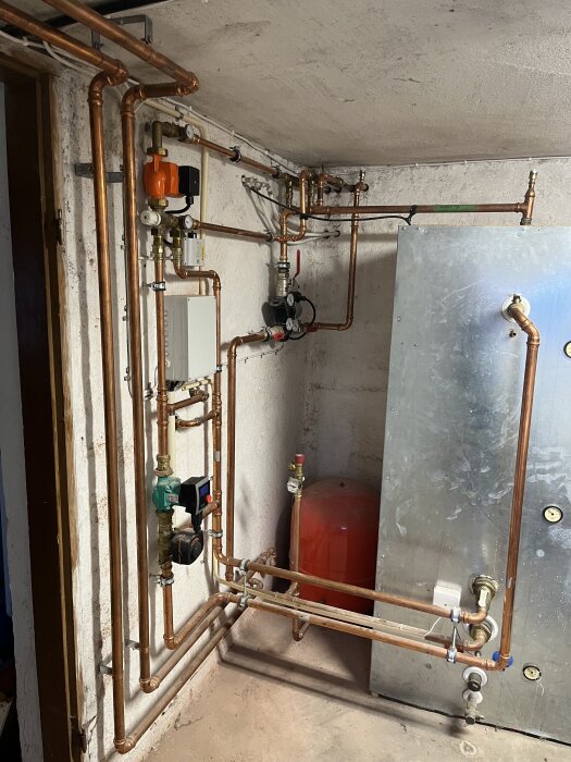 Rörsystem kring vedeldad kamin med laddomat och kopplingar till ackumulatortank i en källare.