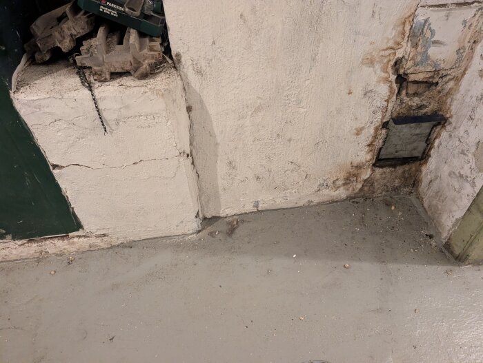 Vägg med sotningslucka, sprickor och smuts vid panna eller skorsten.