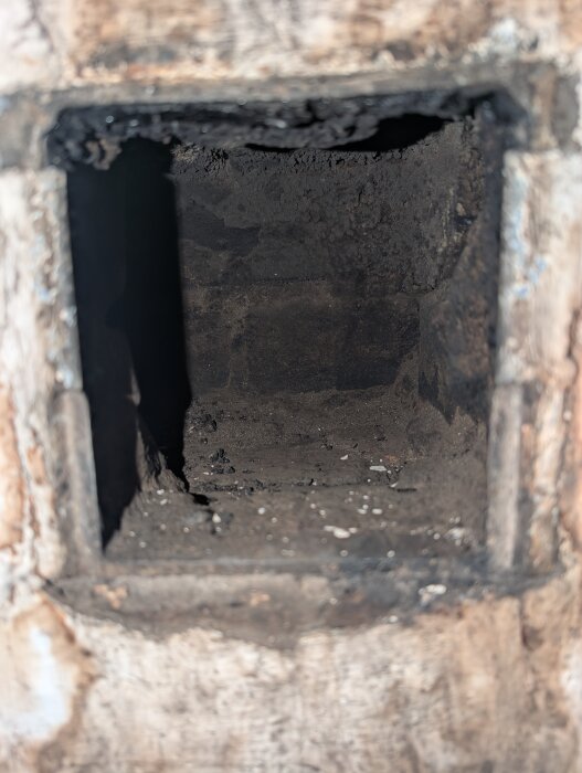 Öppen sotningslucka med inre av skorstenens dunkel, sot och smuts synliga på väggarna.