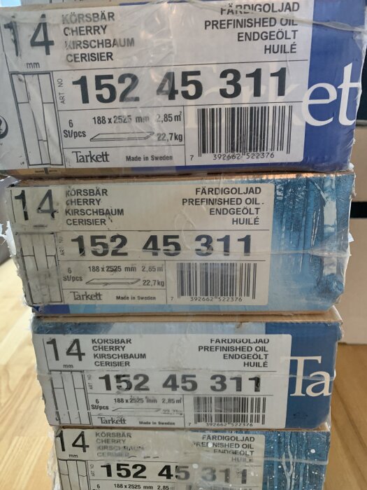 Staplade paket med Tarkett trägolv i körsbär, etiketter visar dimensioner och vikt.