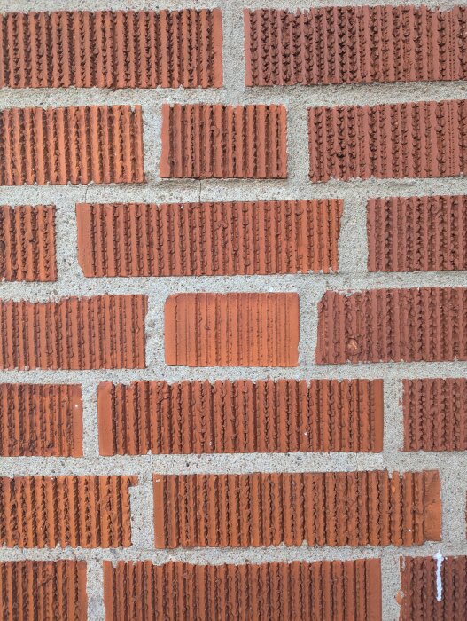 Röda tegelstenar med räfflad yta staplade i ett murverk.