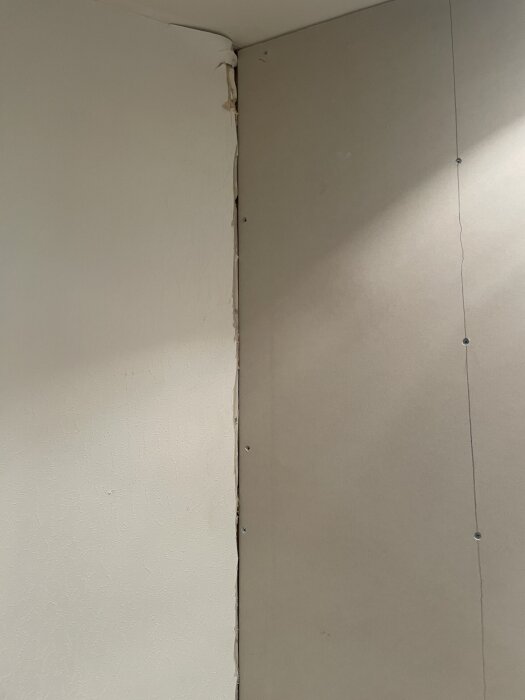 Övergång mellan gammal och ny vägg, med synligt mellanrum och skruvar, där hörnet behöver fyllas innan spackling.
