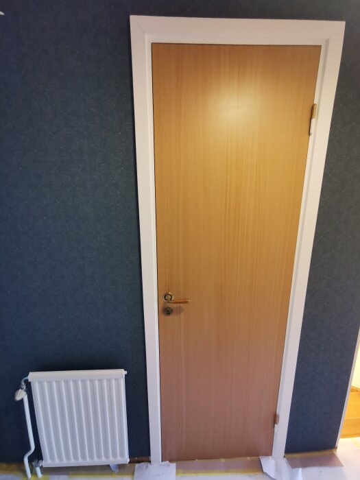 Dörr med träfinish och vit karm omgiven av mörk tapet; radiator bredvid.