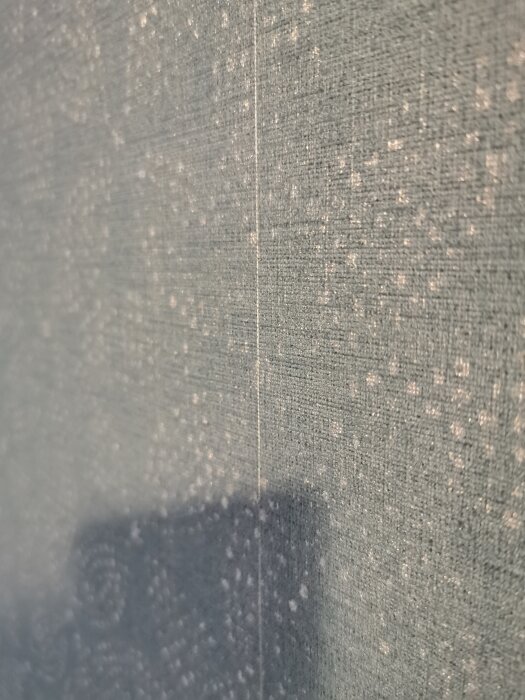 Närbild på en vägg där två tapetkanter möts, med en synlig vit kant mot en mörkare tapetfärg.