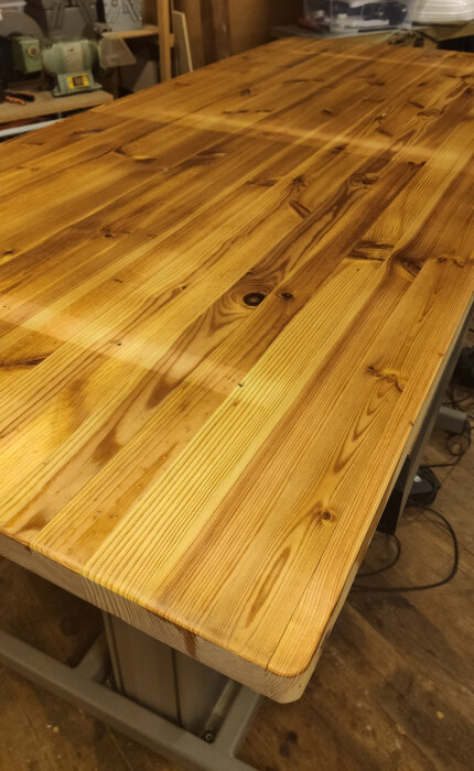 Nybehandlad och slipad träbordsskiva i ett verkstadsutrymme, med synliga träådror och glansig yta.