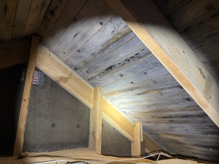 Vind med träbjälkar och brädor, viss missfärgning synlig. Gammal ventilationskanal delvis skymtar, föreslagen del i ventilationsbyte.