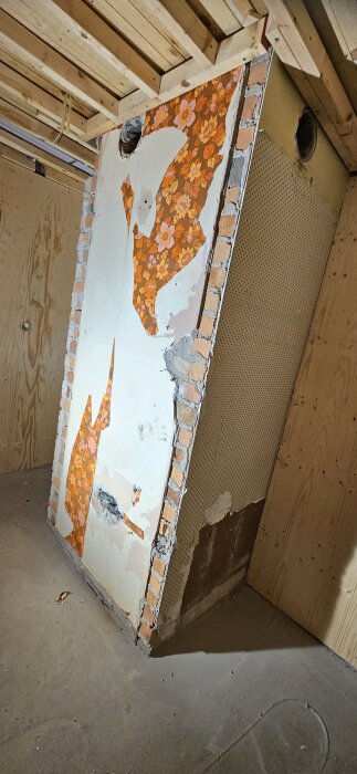 Murstock med orange blomtapet delvis borttagen, tegelstenar synliga på kanterna, ligger i ett badrum under renovering.